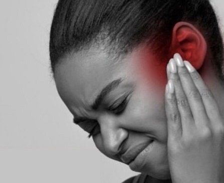 A black woman with her fingers on her left ear presumably in pain from chronic rhinosinusitis